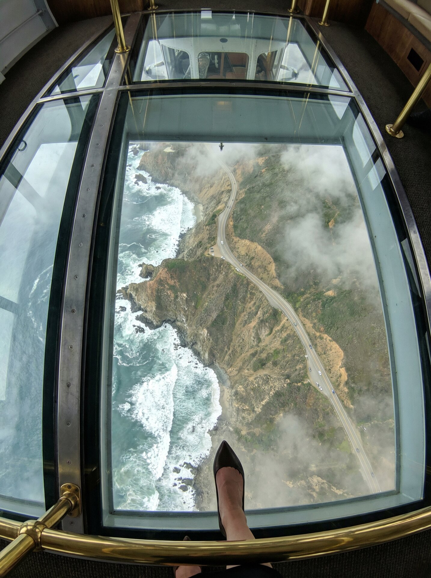 Looking straight down through glass floor, Highway 1 winding 3000 feet below through clouds